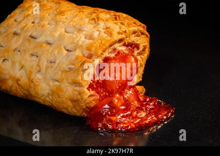 Ein gebackenes Brötchen mit roter Erdbeermarmelade im Elektroofen: Nahaufnahme Stockfoto