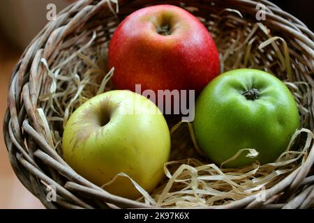 Gelbe, rote und grüne Apfelfrüchte in Holzspäne in Einem Weidentopf Nahansicht Stockfoto Stockfoto