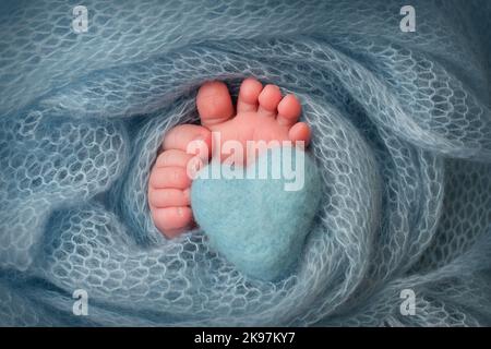 Weiche Füße eines Neugeborenen in einer türkisfarbenen Wolldecke. Nahaufnahme der Zehen, Fersen und Füße eines Neugeborenen. Stockfoto