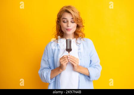 Junge Frau isst leckeres Eis, genießt gefrorenes Dessert, in legerer Kleidung gekleidet, isoliert auf gelbem Hintergrund. Stockfoto