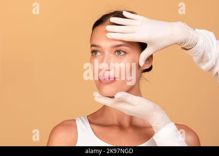 Kosmetologe in Handschuhen, überprüft das Gesicht junger Frauen vor der Schönheitsbehandlung, berührt Stirn und Kinn, kopiert den Raum Stockfoto