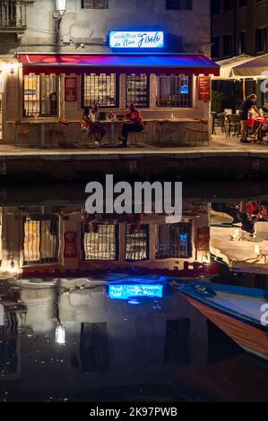 20. August 2022, chioggia, Italien: Touristen genießen die Sommerabende auf den Terrassen der Restaurants entlang des Kanals von Chioggia in Venetien. Chioggia, eine Stadt in der venezianischen Lagune, die viele Touristen beherbergt, die Venedig besuchen, wurde nicht in den venezianischen Stadtkern aufgenommen. Touristen, die dort bleiben, müssen die Steuer jedes Mal zahlen, wenn sie Venedig ab dem 16. Januar 2023 besuchen. (Bild: © Laurent Coust/SOPA Images via ZUMA Press Wire) Stockfoto