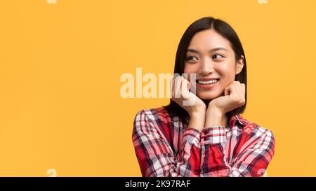 Tolles Angebotkonzept. Hübsche asiatische Dame, die ihre Wangen mit Händen berührt und den Kopierraum auf gelbem Hintergrund betrachtet Stockfoto