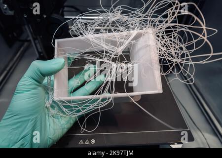 Entfernen eines fehlgeschlagenen 3D-Ausdrucks aus dem Drucker aufgrund einer schlechten Temperatureinstellung und eines Durcheinander von PETG-Filament. Stockfoto