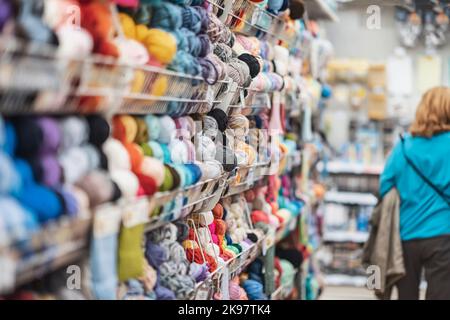 Verschwommener abstrakter Hintergrund des Ladens mit mehrfarbigen Garnknäueln. Stricken und häkeln. Handarbeiten, handgemachtes Konzept Stockfoto