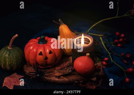 Halloween festliches Layout mit Jack-O-Laterne, Kürbissen, Kerze und Spinne auf Holzschneidebrett auf schwarzem Tisch. Konzept der Herbstferien. Nahaufnahme. Stockfoto