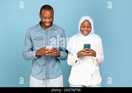 Happy Black Muslim Paar Mit Mobiltelefonen Auf Blauem Hintergrund Stockfoto