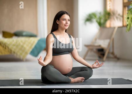Morgenmeditation. Junge Schwangerin praktiziert Yoga in Lotus-Position zu Hause Stockfoto