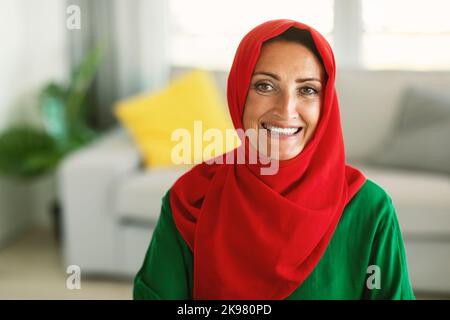 Muslimische Frau Mittleren Alters, Die Traditionelle Hijab Trägt Und Zu Hause Sitzt Stockfoto