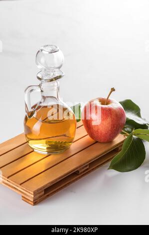 Apfelessig in einer Glasflasche und frische Äpfel mit Blättern auf hellem Hintergrund Stockfoto