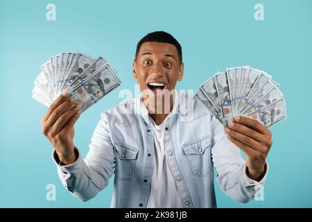 Glücklich inspiriert tausendjährigen afroamerikanischen Mann mit offenem Mund zeigt eine Menge Dollar in den Händen Stockfoto
