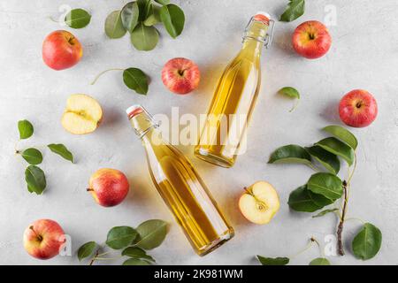 Apfelessig in zwei Glasflaschen und frische Äpfel mit Blättern auf hellem Hintergrund, Draufsicht, flach liegend Stockfoto