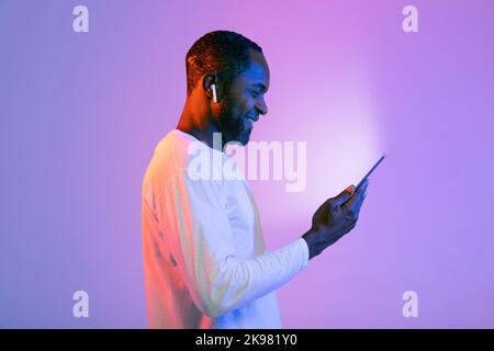 Lächelnder afroamerikanischer Mann, der Kopfhörer und Handy benutzt Stockfoto