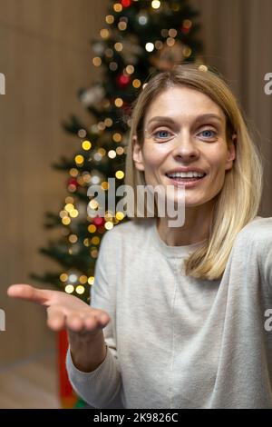 Vertikale Aufnahme, Frau zu Weihnachten im Gespräch auf Videoanruf, um Freunde während der Neujahrsferien online zu begrüßen und zu Hause auf dem Sofa im Wohnzimmer in der Nähe des Weihnachtsbaums zu sitzen. Stockfoto