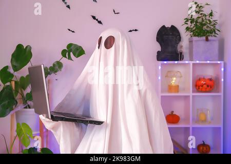 Der Geist von Halloween verwendet einen Laptop, um im Internet zu surfen, um Online-Shops, Märkte zu durchsuchen. Ein Geist macht einen Bestellcomputer für Halloween. Der Geist zahlt für einen Online-Kauf. Neonlicht. Stockfoto