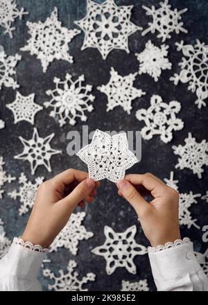 Eine der schönen weißen Baumwolle gehäkelt Stern Schneeflocken in Mädchen Hände als kleines handgemachtes Geschenk oder Dekoration zu Hause. Weihnachts-DIY-Konzept. Draufsicht. Stockfoto