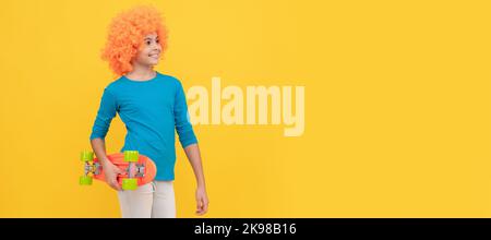 Fröhliches egoistisches Kindermädchen in lockiger Perücke hält Penny Board, Hipster. Lustige Teenager Kind in Perücke, Party-Poster. Banner-Kopfzeile, Kopierbereich. Stockfoto