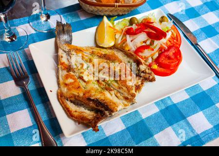 Gebratene dorada mit Pesto, serviert mit Gemüsegarnitur und Zitrone Stockfoto