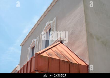 Rendering auf der Außenseite eines historischen Gebäudes mit zwei Fenstern. An der Außenwand befinden sich dicke weiße Zierleisten und Fensterläden sowie ein Kupferschirm. Stockfoto
