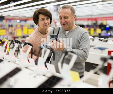 Reifer Mann und Frau, die sich für ein Smartphone im Elektronikgeschäft entscheiden Stockfoto