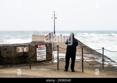 Ein Mann blickt auf den Pier des Hafens von Porthleven, der aufgrund des rauen Wetters gesperrt ist Stockfoto