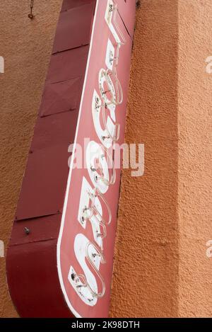 Ein rotes Vintage Tony's Liquor beleuchtete Retro-Schild an der Außenseite eines orangefarbenen Ziegelgebäudes. Das alte Neonschild hängt über einem Schnapsgeschäft Stockfoto