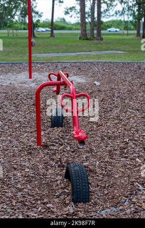 Farbenfrohe, strapazierfähige Kinderspielplätze, Wippe oder Wippe aus rotem Metall in einem Park. Die Spielplatzausrüstung bewegt sich mit einem auf- und abwärts Stockfoto