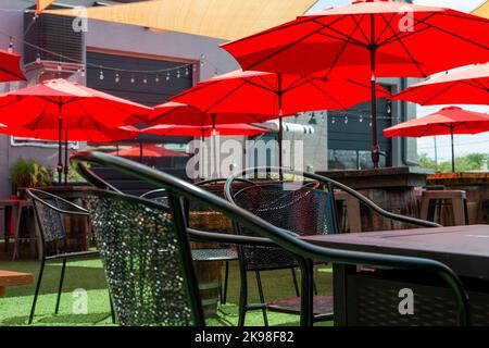 Mehrere dreieckige gelbe Nylonschirme und Markisen, die über einer Terrasse hängen. Es gibt rote Sonnenschirme aus Leinwand, die mit Saiten aufgehängt sind Stockfoto