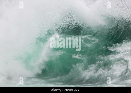 Eine wütende blaugrüne Farbe, massive Wellen einer Welle, während ihr Fass entlang des Ozeans rollt. Der weiße Nebel und der Schaum der Welle sind schaumig und flauschig. Stockfoto