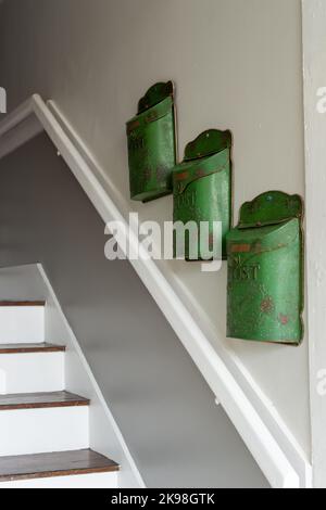 Drei grüne Metallpostfächer, Briefkästen oder Briefkästen wurden an einer weißen Innenwand des Wohngebäudes angebracht. Sie sind in einer Kaskade angeordnet. Stockfoto