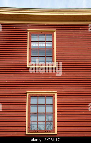 Das Äußere eines rot gefärbten Häuschens mit einer Holzwand, die mit einer horizontalen Klappwand bedeckt ist. Es gibt zwei Vintage-Fenster mit mehreren Glasscheiben Stockfoto