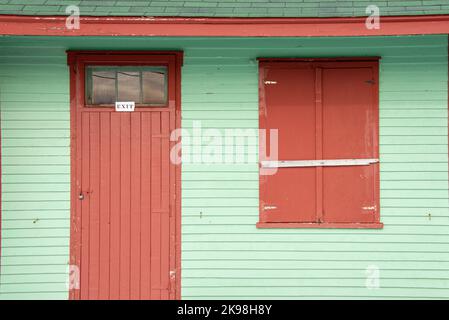 Ein leuchtendes Minzgrün bemalte das Äußere eines Gebäudes mit einer hölzernen Fenstertür und einem geschlossenen Fenster mit zwei Fensterläden. Es gibt einen kleinen weißen Ausgang Stockfoto