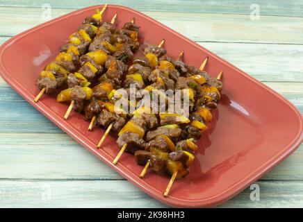 Gekochte Spieße aus Rindfleisch und gelber Paprika und Gemüse mit grünen Zwiebeln auf roter Servierplatte Stockfoto