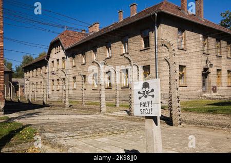 Stopp-Warnschild vor einem elektrifizierten Stacheldrahtzaun und Gebäude im ehemaligen Nazi-Konzentrationslager Auschwitz I, Auschwitz, Polen. Stockfoto
