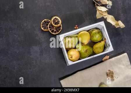 Stillleben mit Holzkiste mit Birnen, getrocknete Orangenscheiben auf dunkelgrauem Hintergrund Stockfoto