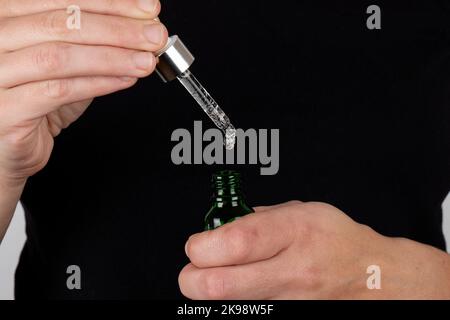 Die Hand hält eine Pipette und eine Flasche Medizin in den Händen. Stockfoto