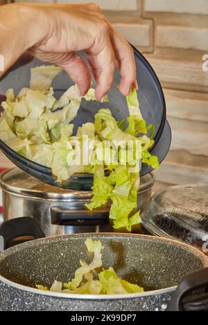 Der Koch wirft Salat in den Topf auf den Gasherd Stockfoto