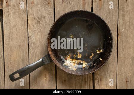 Alte schmutzige Bratpfanne nach dem Essen steht auf einem Holztisch, Nahaufnahme, Küchenutensilien Stockfoto