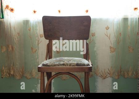 Der alte braune Stuhl steht im Schlafzimmer in der Nähe des Fensters aus der Nähe Stockfoto