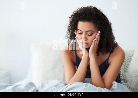 Ich bin einfach so müde. Eine attraktive junge Frau, die unter Kopfschmerzen leidet und sich im Bett den Kopf reibt. Stockfoto