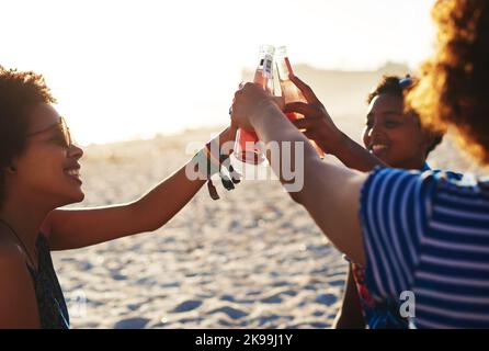 Cheers to the weekend. Ein attraktives junges Trio von Frauen feiern und trinken zusammen am Strand während des Tages. Stockfoto