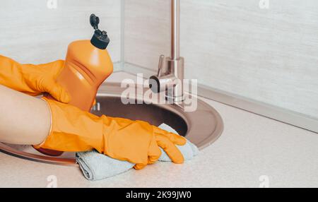 Hand in orangefarbenem Gummihandschuh mit Mikrofaser-Reinigungstuch und Flasche mit Sterilisationslösung für Reinigung und Desinfektion. Reinigung, Desinfektion k Stockfoto