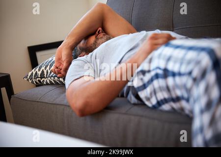 Wird sein Tag noch schlimmer? Ein reifer Mann, der erschöpft aussieht, während er morgens zu Hause auf einer Couch liegt. Stockfoto