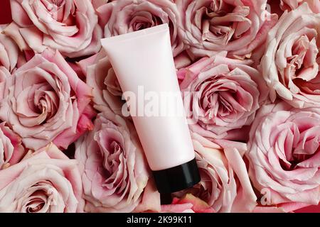 Unbranded rosa Squeeze Flasche cremefarbenen Rohr mit schwarzem Schraubverschluss und rosa Rosen Hintergrund. Flasche für Branding und Etikett. Natürliche Bio-Wellness-Kosmetik. Stockfoto