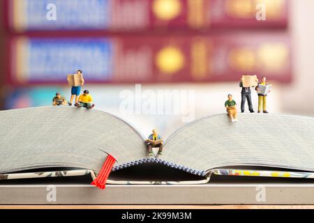 Nahaufnahme von Miniaturfiguren einer Gruppe von Menschen, die Buch und Zeitung lesen. Stockfoto