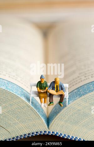 Nahaufnahme von Miniaturfiguren eines älteren Paares, das Buch und Zeitung auf einer Bank las. Stockfoto