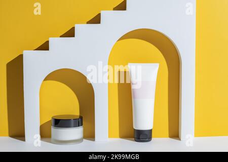 Kosmetische Schönheitsprodukte in weißem Bogen auf gelbem Hintergrund. Nicht markengeschützte Verpackung adv. Cremedose und Tube. Stockfoto