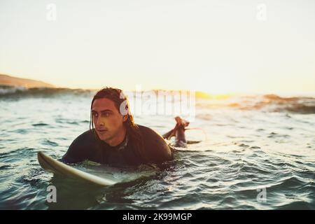 Steigen Sie mit der Flut auf und gehen Sie mit der Strömung. Ein junger Mann, der auf einem Surfbrett im Meer paddelt. Stockfoto