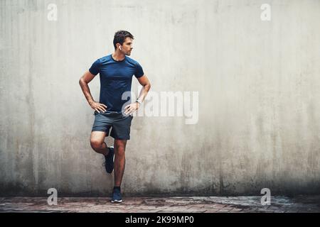 Je mehr Herausforderungen Sie ertragen, desto mehr werden Sie sich verändern. Ein sportlicher junger Mann, der beim Training im Freien an einer grauen Wand steht. Stockfoto