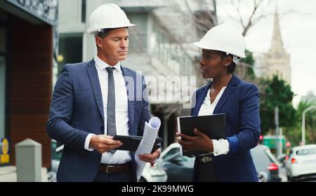 In dieser Stadt wuchsen unsere Geschäfte. Zwei Geschäftsleute, die Harthüte trugen, diskutierten draußen in der Stadt. Stockfoto